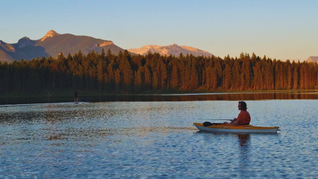 Angler on a beautiful mountain lake fishing from a kayak at sunset